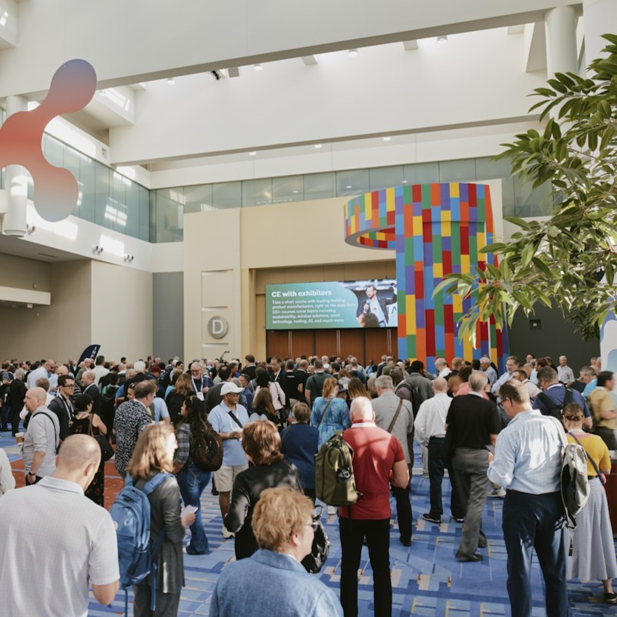 A large crowd of conference attendees gathers in a bright, spacious convention center lobby with colorful signage and modern architectural elements.